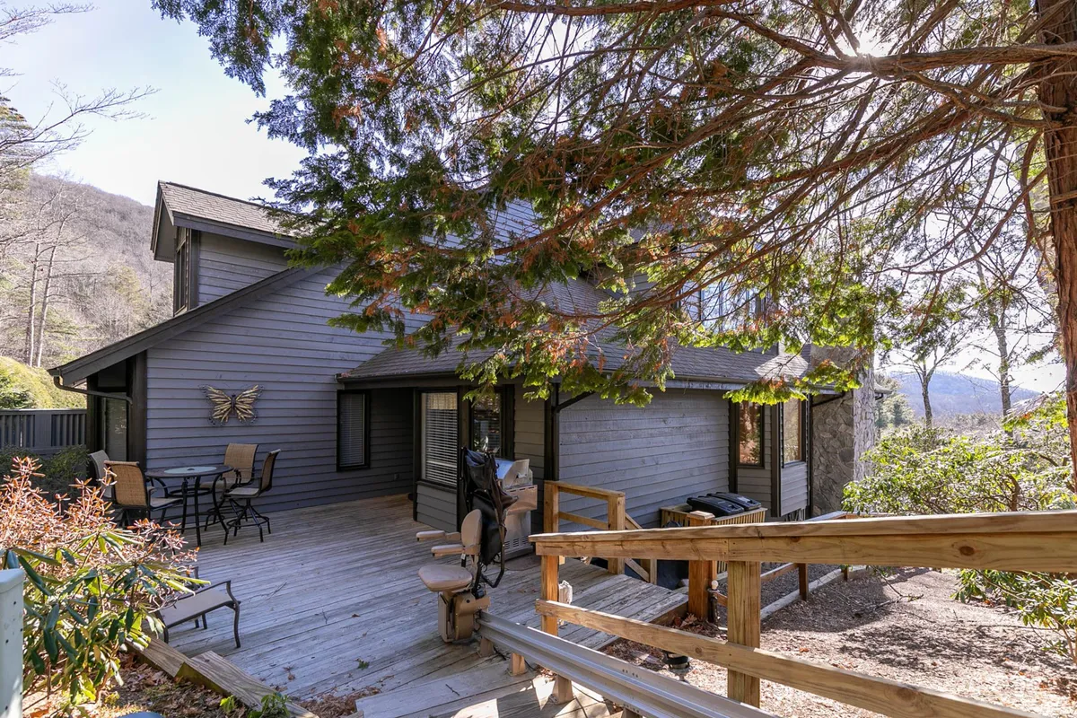 A tranquil wooden deck with comfortable seating overlooks a sweeping mountain view, surrounded by lush trees. The outdoor space invites relaxation, social gatherings, and immersion in nature—capturing the essence of resort living just outside your door.