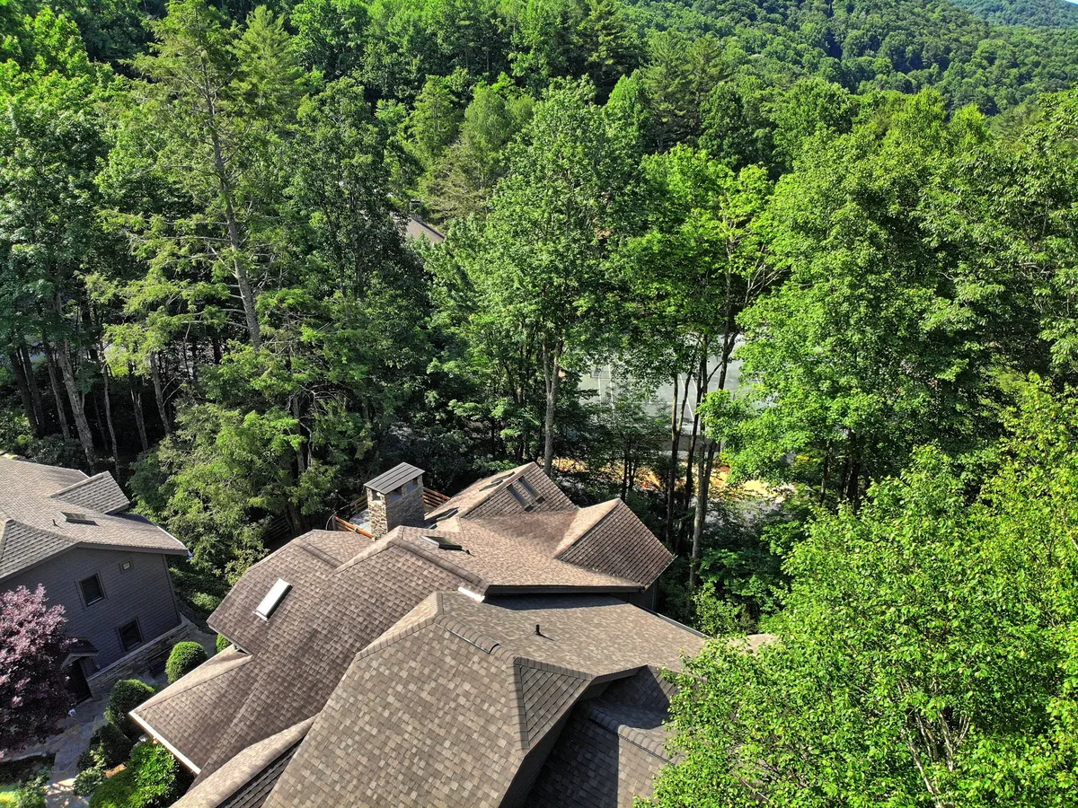An elevated view reveals rooftops of neighboring houses nestled in dense greenery, with distant hills and forests in the background. The scene evokes the communal and natural setting of the resort neighborhood, suggesting proximity to shared amenities.