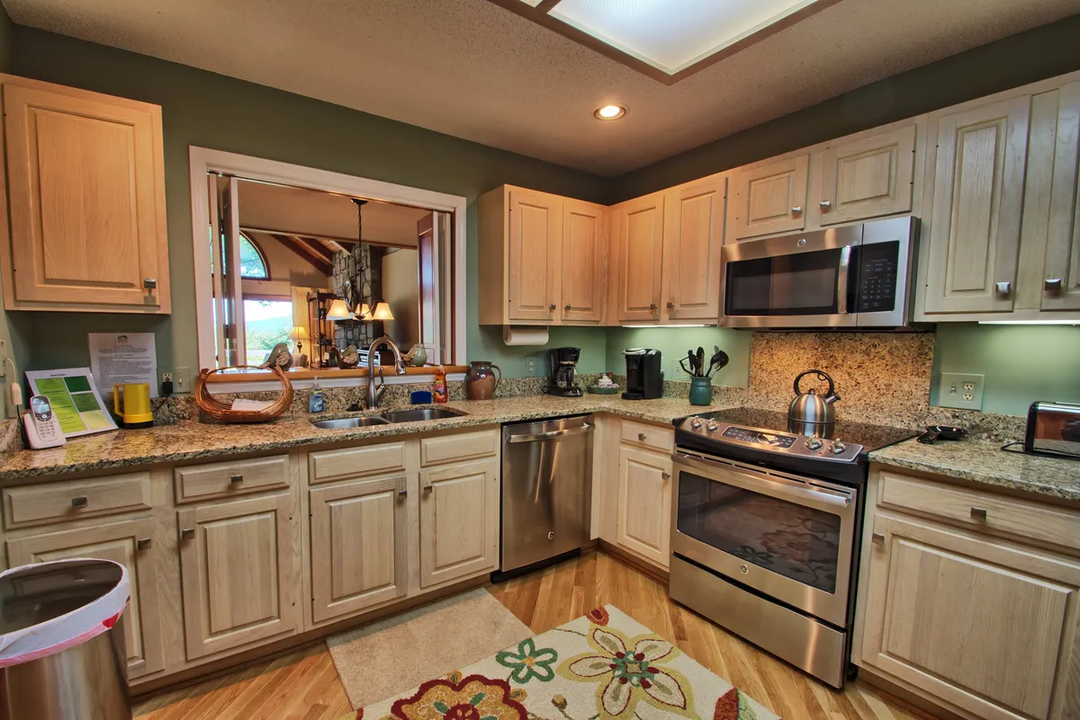A close-up angle of the kitchen, focusing on granite countertops, modern appliances, and a vibrant rug. A window with a scenic view brings in daylight, and the practical layout is ideal for cooking and entertaining.