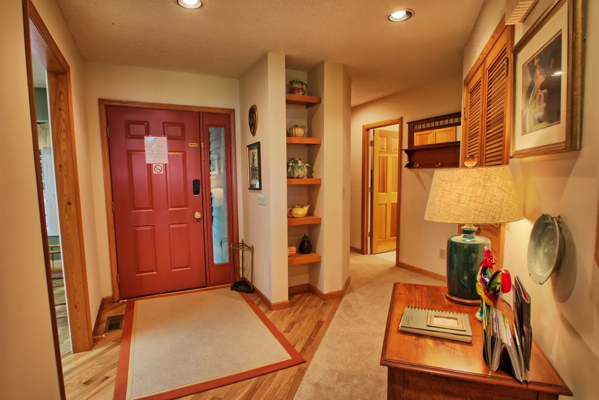 The welcoming entryway of the townhome, with a bold red front door, a decorative side table with a lamp and magazines, and shelves with thoughtful decor. The scene radiates warmth and hospitality as you step inside.