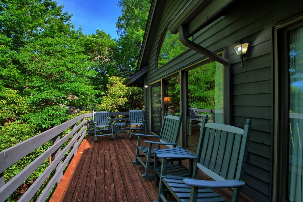 An inviting wooden deck stretching along the house, furnished with classic rocking chairs and surrounded by lush greenery. The view opens toward distant mountains, offering a serene setting for morning coffee or evening relaxation.