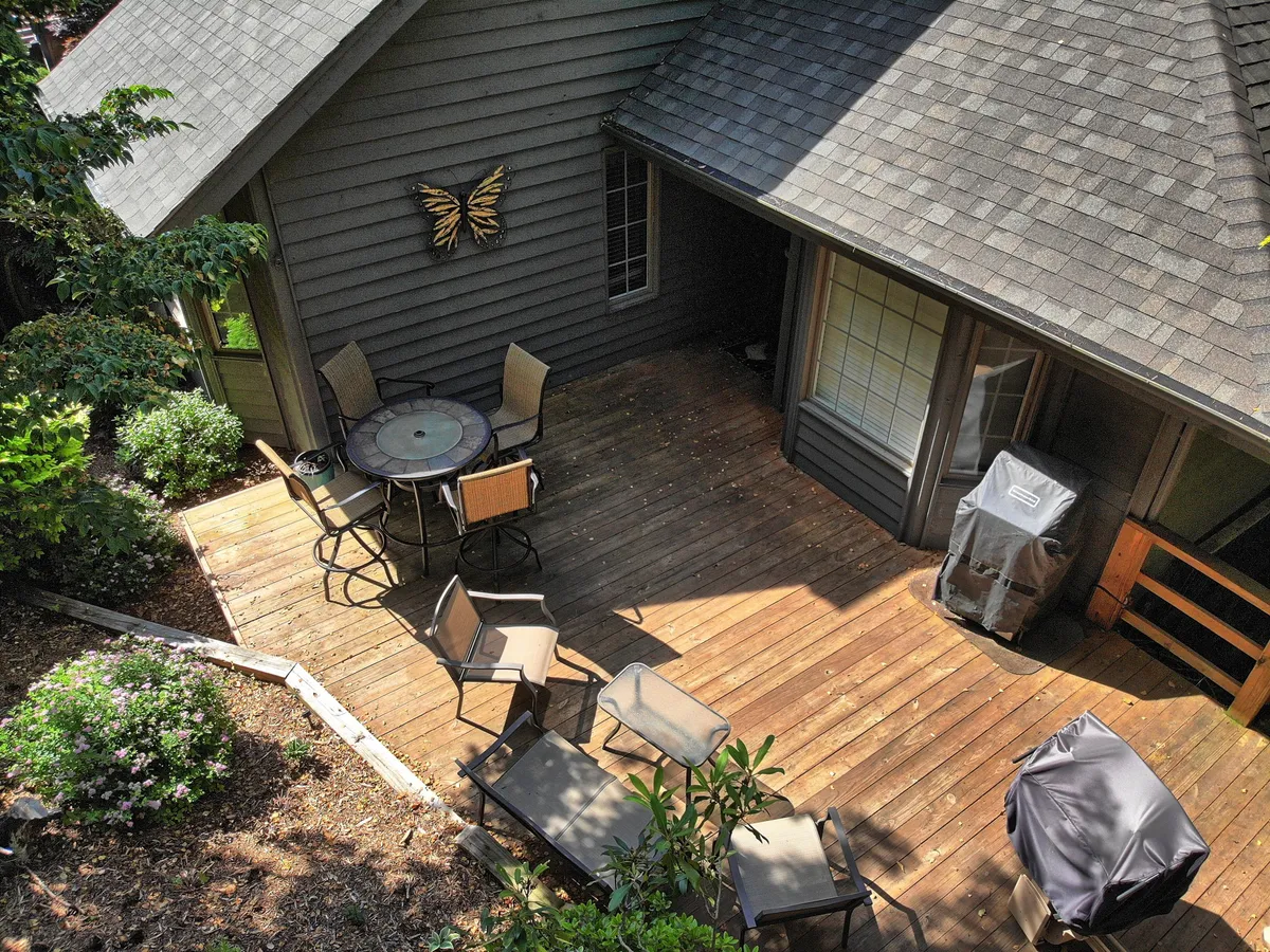 An inviting outdoor seating area featuring a dining table surrounded by comfortable chairs. The scene includes a butterfly wall decoration and a grill, all set on a spacious wooden deck overlooking natural greenery. The space is ideal for relaxing, sharing meals, or enjoying the fresh mountain air after a day of local adventures.
